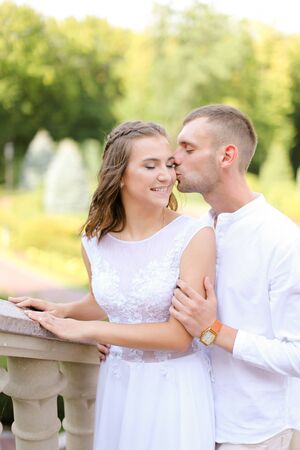 Happy beautiful bride and groom holding each other, kissing and standing outdoors. Concept of relationship, wedding and bridal photo session.の写真素材