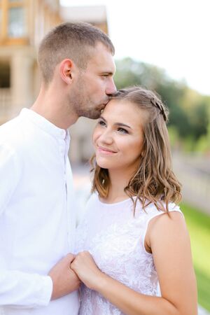 Caucasian groom kissing bride and holding hands outdoors. Concept of wedding and bridal photo session, relationship.の写真素材