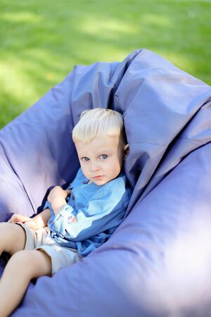 Little blond male child sitting in bag chair on grass. Concept of chi dhood.の写真素材