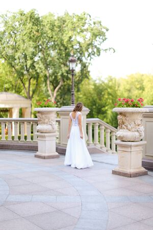 Back view of oung bride walking outside in white nice dress. Cponcept of wedding day, fiancee.の写真素材