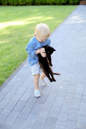 Little blond playing with black cat outdoors. Concept of childhood and pets.の写真素材