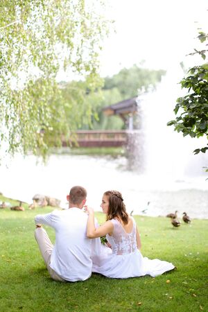 Handsome groom and fiancee sitting near lake and resting. Concept of married couple and nature.の写真素材