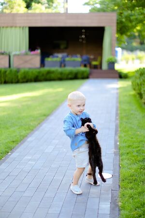 Little boy in jeans shirt standing with cat in yard. Concept of kids, childhood and pets.の写真素材