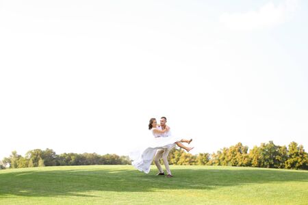Groom holding bride on grass in white sky background. Concept of wedding photo session on nature.の写真素材