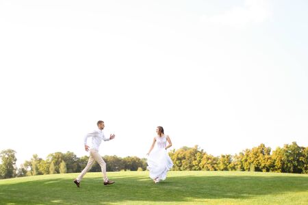 Groom and pretty bride running and playing on grass. Concept of wedding photo session on open air and nature.の写真素材