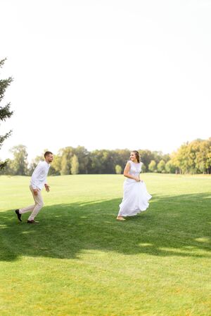 American groom and bride running and playing on grass. Concept of wedding photo session on open air and nature.の写真素材