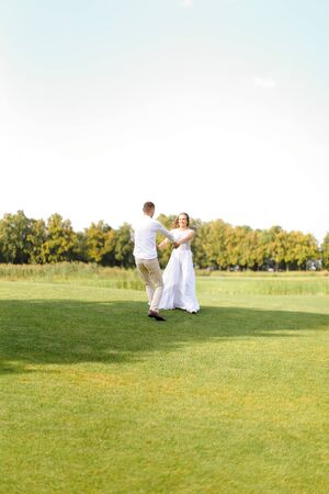 Happy groom and bride dancing on grass. Concept of wedding photo session on open air and nature.の写真素材