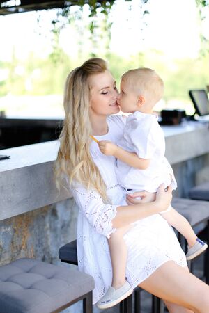 Young mother holding baby outside and wearing white clothes. Concept of motherhood and child.の写真素材