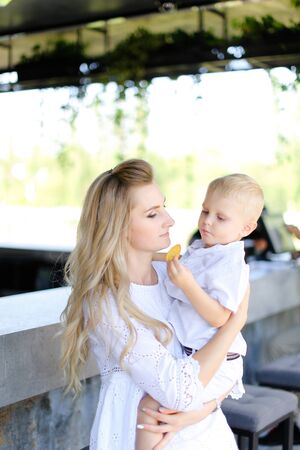 Young caucasian mother holding baby outside and wearing white clothes. Concept of motherhood and child.の写真素材