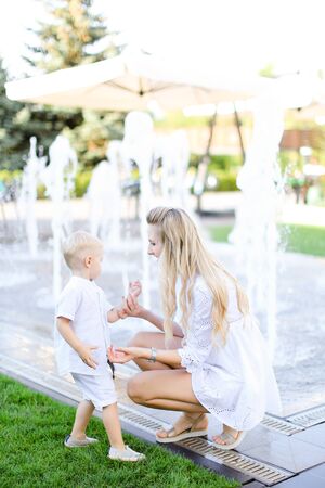 Young mother playing with little baby outside near fountain. Concept of walking in city and motherhood.の写真素材