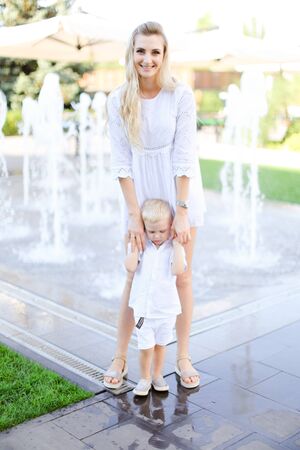 Young smiling mother walking with little baby outside near fountain. Concept of walking in city and motherhood.の写真素材