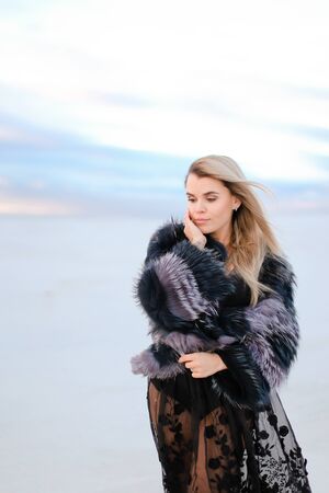 Young caucasian girl wearing black dress standing in white snowed steppe background. Concept of fashion and winter photo session.の写真素材