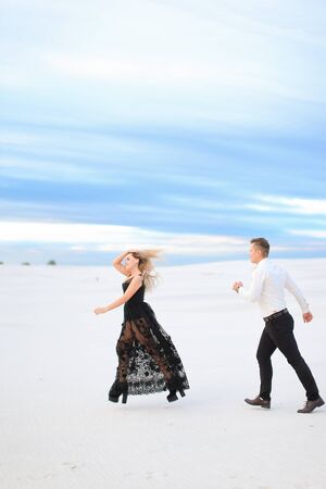 Young female person and man running on snow, wearing black transparent dress. Concept of winter photo session and happy couple.の写真素材