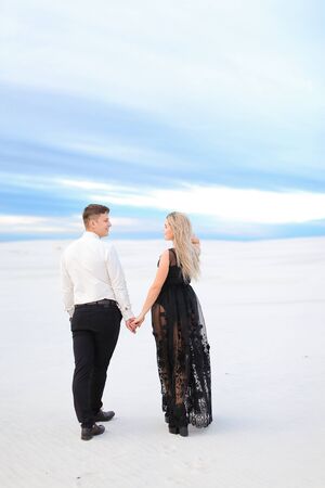 Back view of young girl in black transparent dress holding man hands and walking in winter steppe. Concept of seasonal photo session and love.の写真素材
