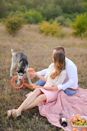 Young happy woman and man sitting on grass plaid and playing with husky. Concept of picnic on nature and dogs.の写真素材
