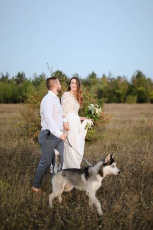 Groom walking with fiancee and dog in steppe, holding hands. Concept of happy married couple and love.の写真素材