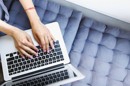Hands texting on laptop keyboard in blue pillows background. Concept of buying property online.の写真素材