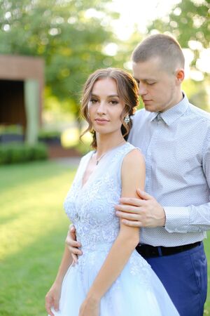 Happy groom hugging fiancee in park, sun rays. Concept of bridal couple and wedding photo session in open air.の写真素材