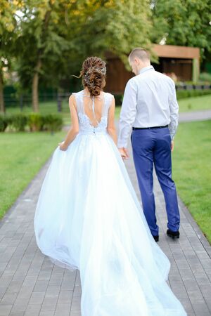 Back view of caucasian bride and groom going outdoors. Concept of wedding photo session outside and happy bridal couple walking in garden.の写真素材
