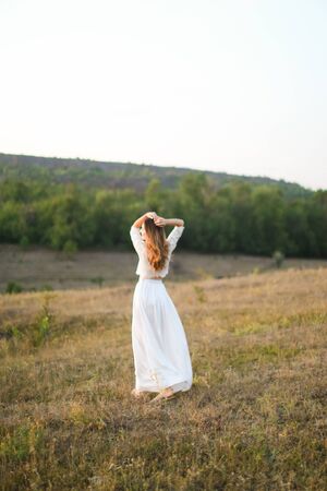 Caucasian european woman walking in steppe and wearing white dress. Concept of nature, bridal photo session on nature and beauty.の写真素材