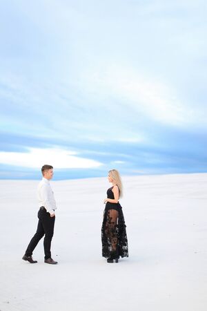Young man in white shirt and woman wearing black transparent dress walking on snow. Concept of winter photo session, relationship and love, happy couple.の写真素材