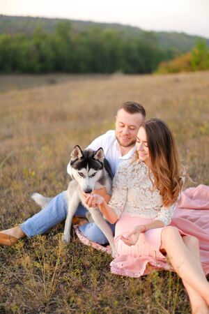Young woman and man sitting on gras with malamute. Concept of relatonship, picnic and dog.の写真素材