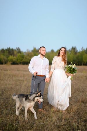 Groom and caucasian fiancee walking in steppe with dog husky. Concept of wedding and bridal photo session with pets on nature.の写真素材