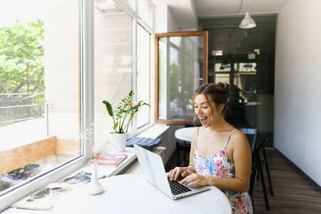 Young happy woman sitting at cafe and surfing internet by laptop. Concept of freelance job and home business.の写真素材