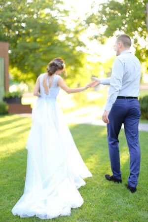 Back view of caucasian bride and groom walking in garden on green grass. Concept of wedding and bridal photo session.の写真素材