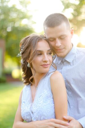 Happy handsome groom hugging fiancee in park, sun rays. Concept of bridal couple and wedding photo session in open air.の写真素材