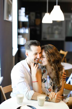 Young happy husband hugging wife and sitting at cafe, drinking coffee. Concept of enjoing togetherness and having lunch.の写真素材