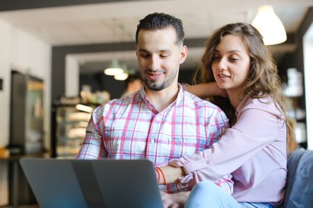 Young smiling woman and man using laptop at cafe and surfing. Concept of free hotspot and fast internet, modern technology and happy couple.の写真素材