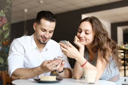 Young wife sitting with husband and using smartphone at cafe. Concept of food and drink, happy couple and relationship, modern technology.の写真素材
