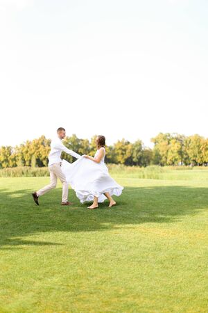 Groom and bride dancing on grass. Concept of wedding photo session on open air and nature.の写真素材