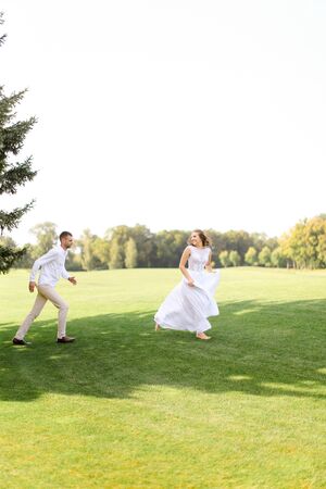 Groom and caucasian bride running and playing on grass. Concept of wedding photo session on open air and nature.の写真素材
