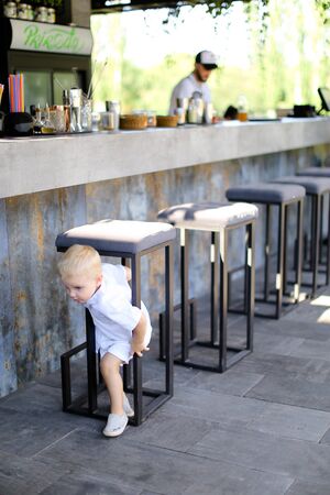 Little cute male baby wearing white clothes and playing outside at street cafe. Concept of childhood.の写真素材