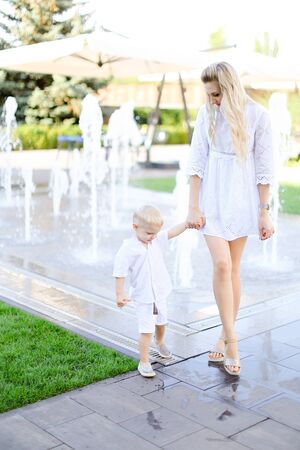 Young caucasian mother walking with little baby outside near fountain. Concept of walking in city and motherhood.の写真素材