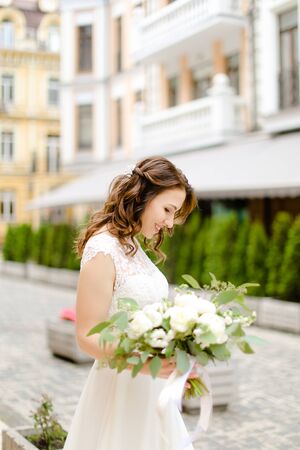 Caucasian happy fiancee walking with bouquet of flowers in city. Concept of bridal photo session.の写真素材