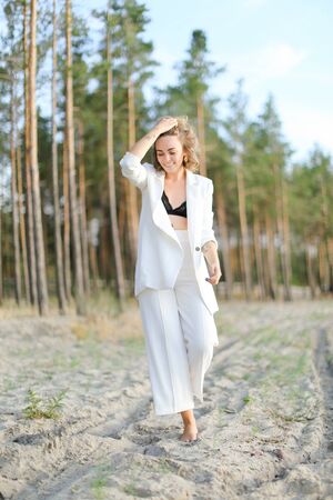 Blonde cute girl walking on sand beach and wearing white clothes. Concept of summer vacations.の写真素材