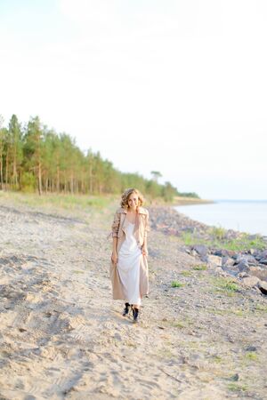 Caucasian girl walking on shingle beach and wearing summer coat. Concept of seasonal fashion and summer vacations.の写真素材