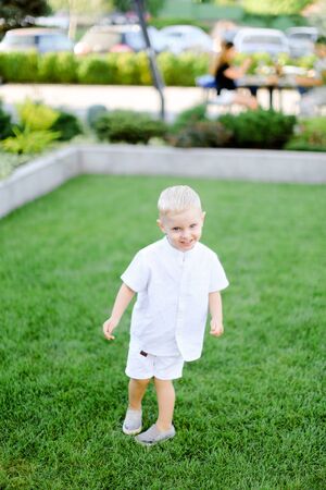 Little child standing on grass and wearing white clothes. Concept of childhood and summer.の写真素材