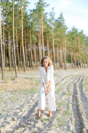 Blonde caucasian girl walking on sand beach and wearing white clothes. Concept of summer vacations.の写真素材