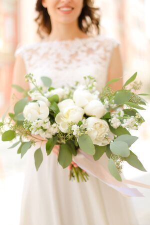 Happy smiling fiancee keeping bouquet of flowers and wearing white dress. Concept of bridal photo session and wedding.の写真素材