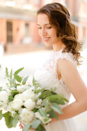 Happy pretty fiancee keeping bouquet of flowers and wearing white dress. Concept of bridal photo session and wedding.の写真素材