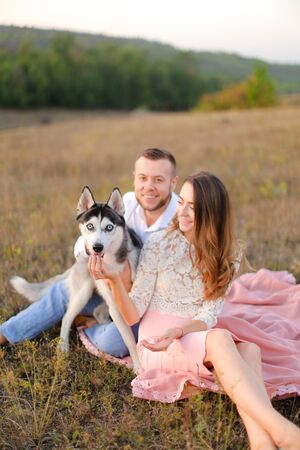 Young girl and man sitting on gras with malamute. Concept of relatonship, picnic and dog.の写真素材