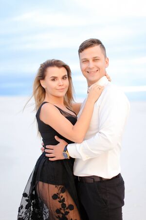 Young caucasian female person wearing black transparent dress hugging man in snow field background. Concept of love and winter photo session.の写真素材