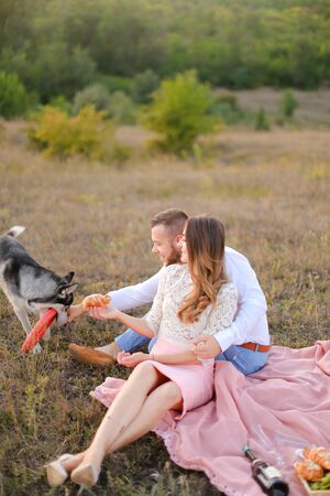 Young caucasian woman and man sitting on grass plaid and playing with husky. Concept of picnic on nature and dogs.の写真素材