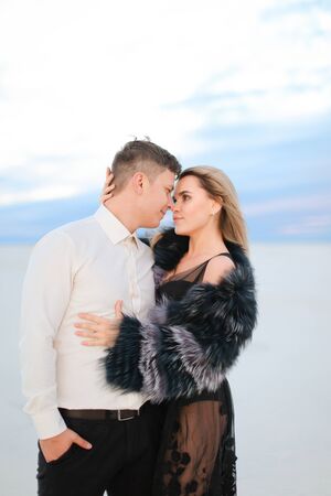 Young blonde woman wearing fur coat hugging man in snowed steppe. Concept of winter photo session and love.の写真素材