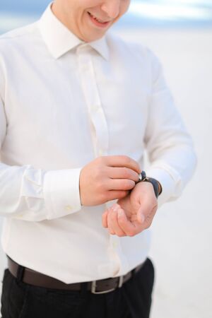Young smiling male person standing in winter steppe and looking at watch. Concept of waiting and seasonal photo session.の写真素材