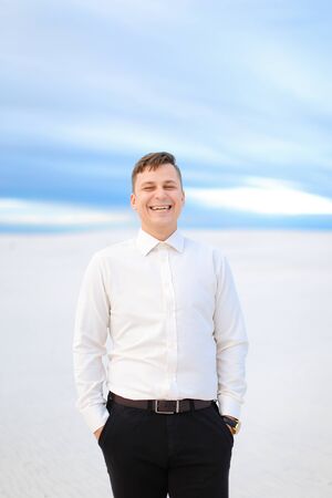 Young smiling male person standing in winter steppe and wearing white shirt, snow in backgrounf. Concept of seasonal photo session.の写真素材